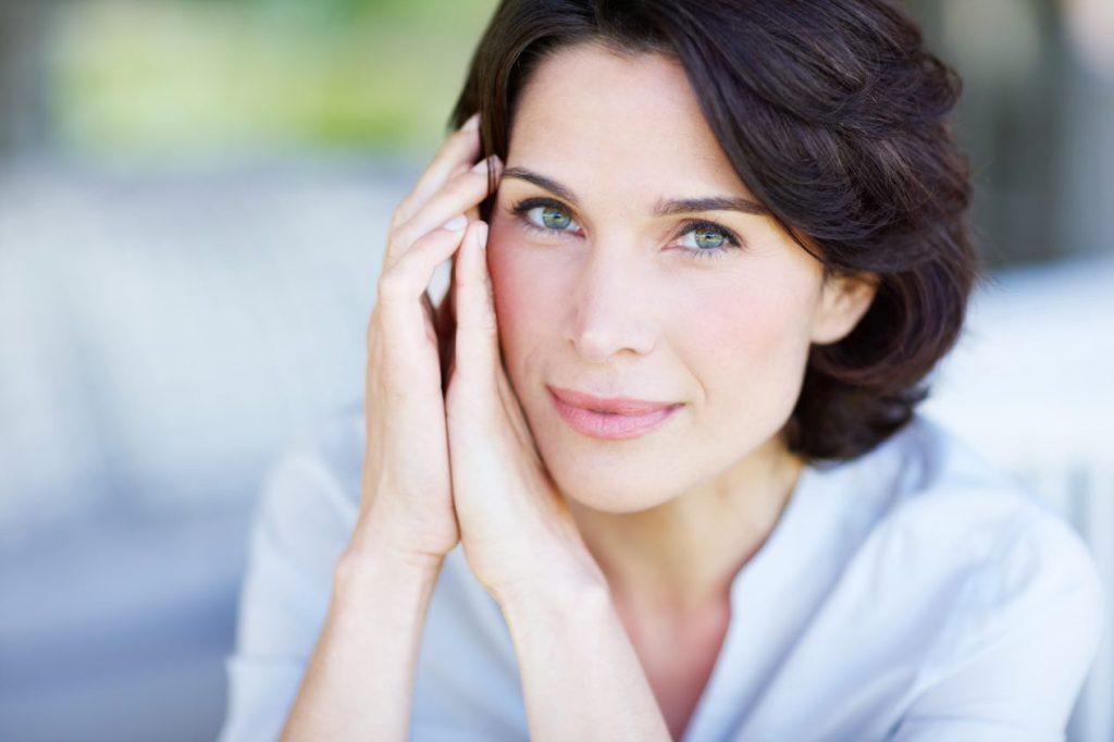 Pretty woman rests the side of her face on her hands and looks at the camera