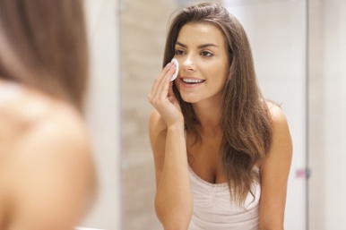 College aged woman looking in mirror and cleaning her face