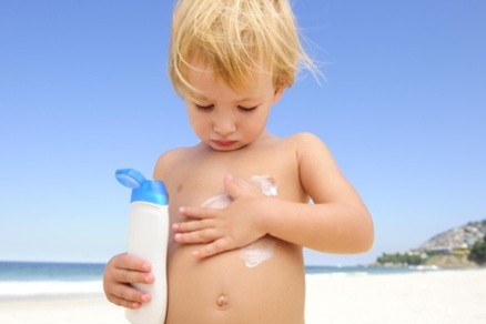 Young boy rubbing sunscreen on his belly at the beach