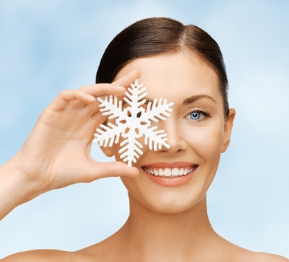 Model with flawless skin holding plastic snowflake in front of her eye