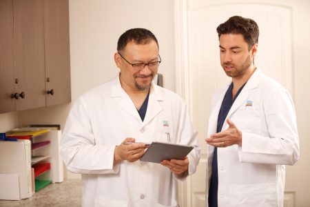 Dr. Tu and Dr. Weitz, both in white lab coats, have a discussion while looking at a tablet.
