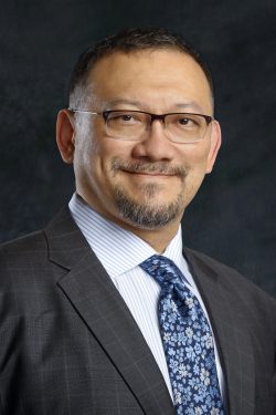 Head shot of Dr. Tu, who is wearing a charcoal suit, blue and white pinstriped shirt, and blue floral tie