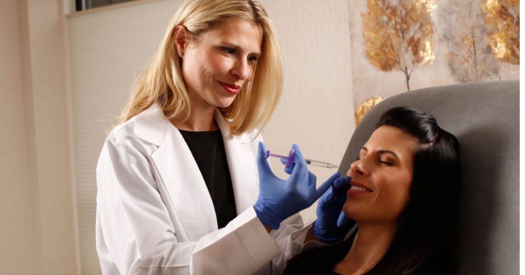 Nurse practitioner Malgorzata Sass performs a dermal fillers treatment, holding the syringe to the patient's face.