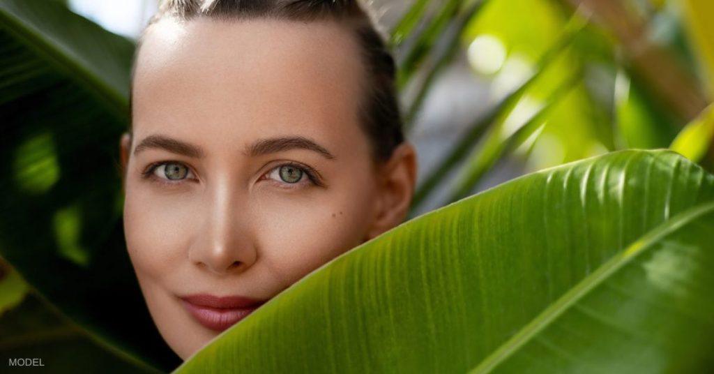 Beautiful young woman with braided hair (model) against fresh green tropical palm and banana leafs.