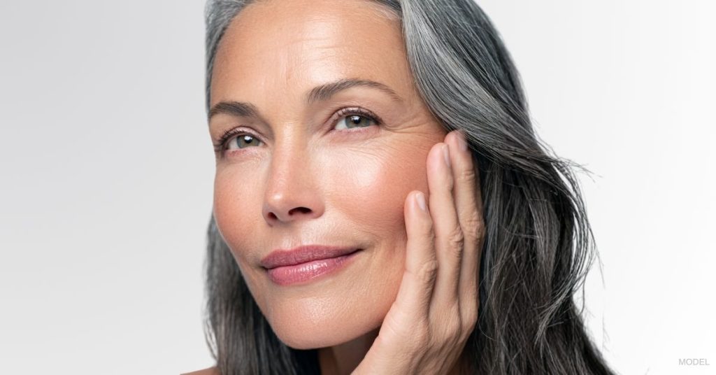 Mature woman smiling and holding her face. (Model)