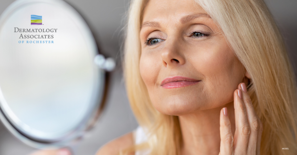 Mature woman (model) touching her cheek while holding a round mirror. Dermatology Associates of Rochester logo.
